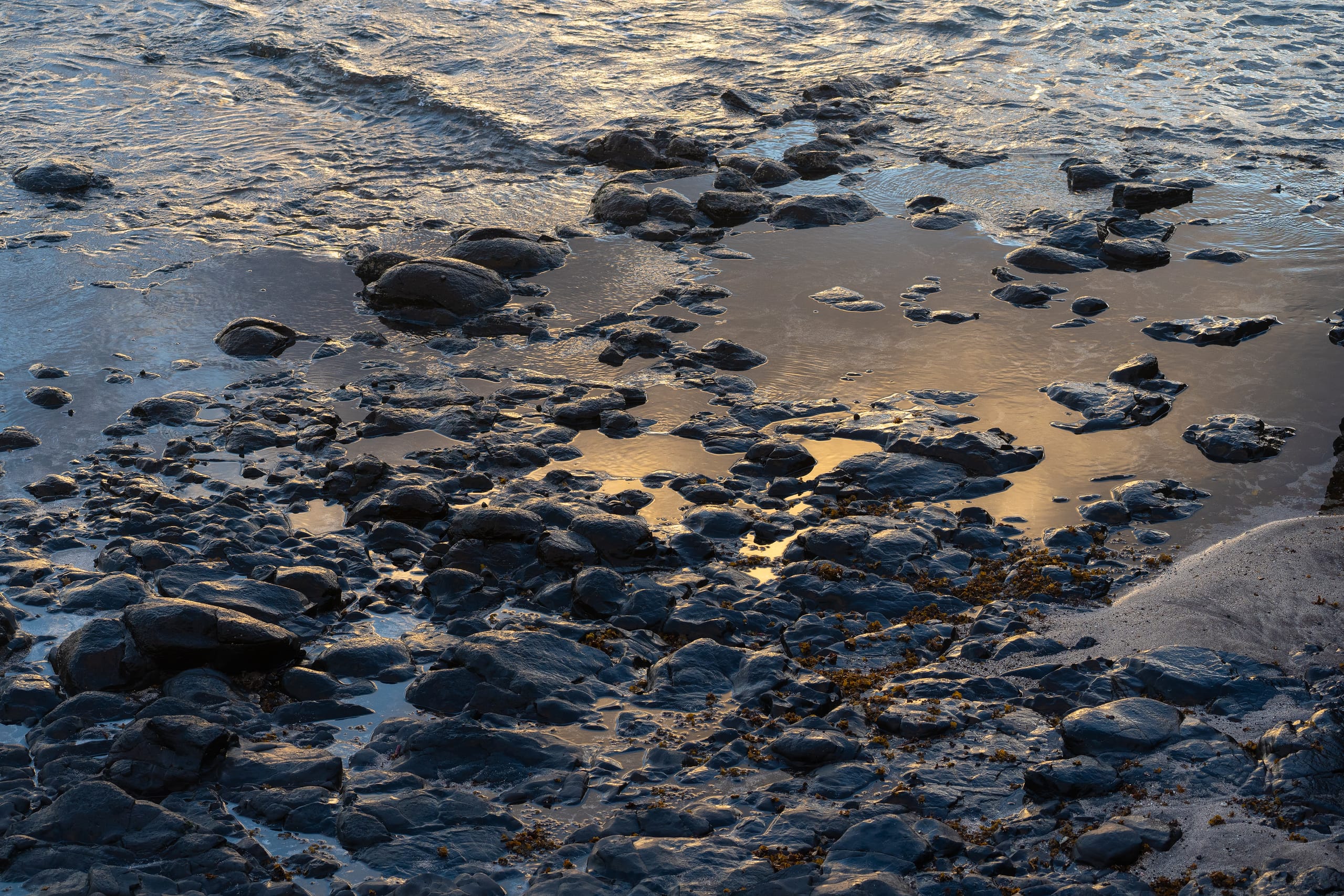 Wet volcanic rocks and pebbles on Gran Canaria shoreline at low tide